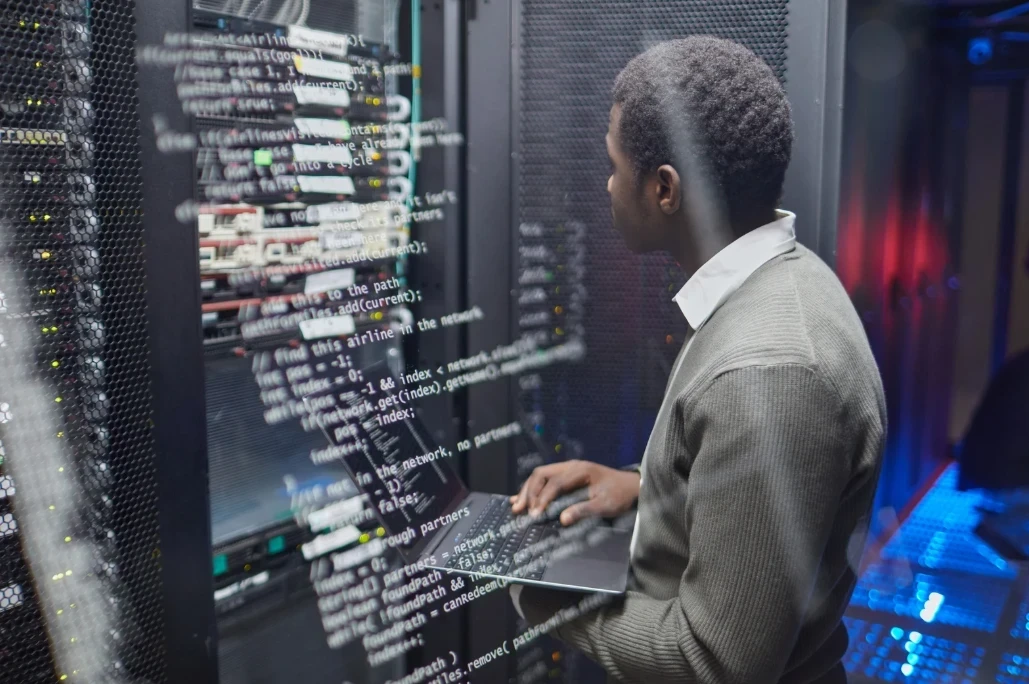 Network engineer working on a laptop beside server racks in a data center